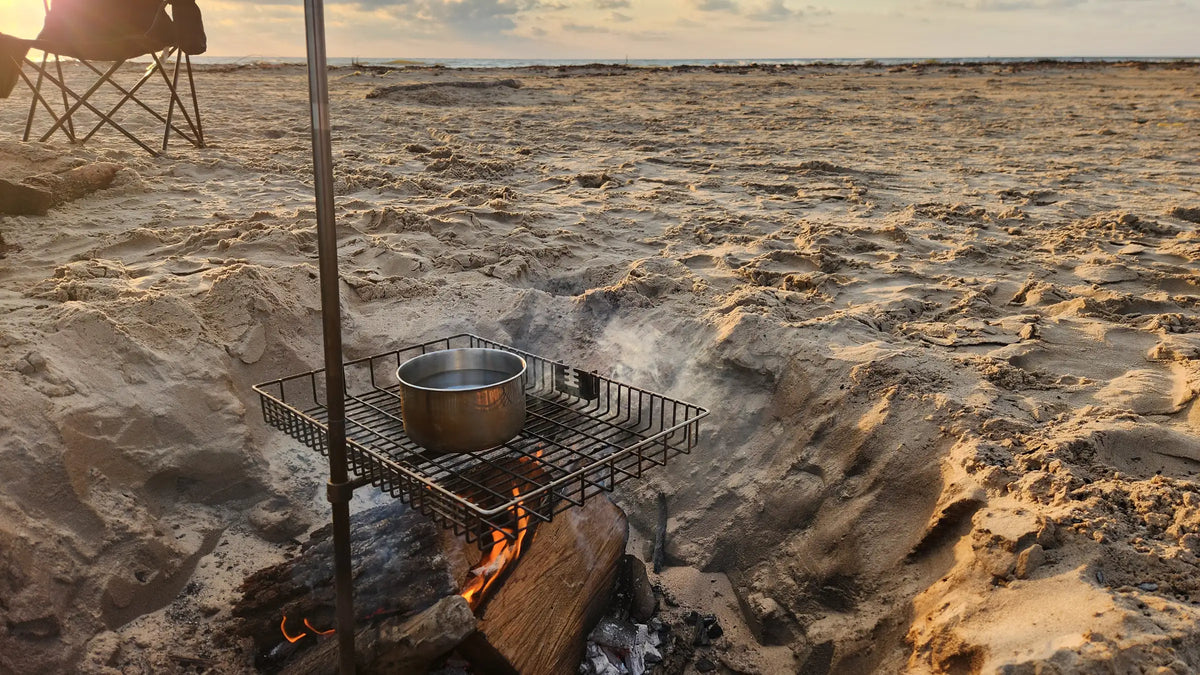 Tyrux Campfire Grill over a beach campfire at sunrise, with a pot on the grill basket