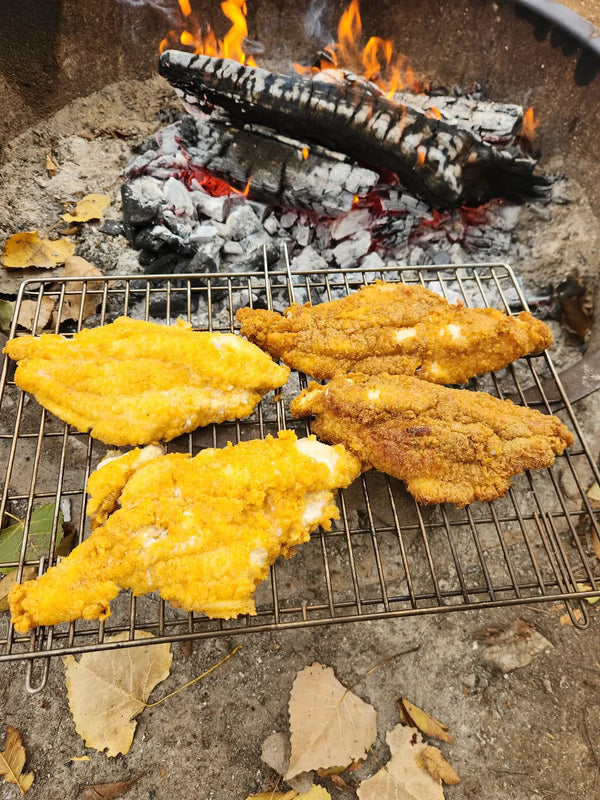 Fried fish fillets in the Tyrux Campfire Grill basket over a campfire