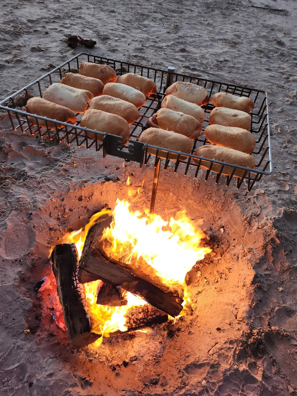 Bread rolls toasting in the Tyrux Campfire Grill basket over a beach campfire